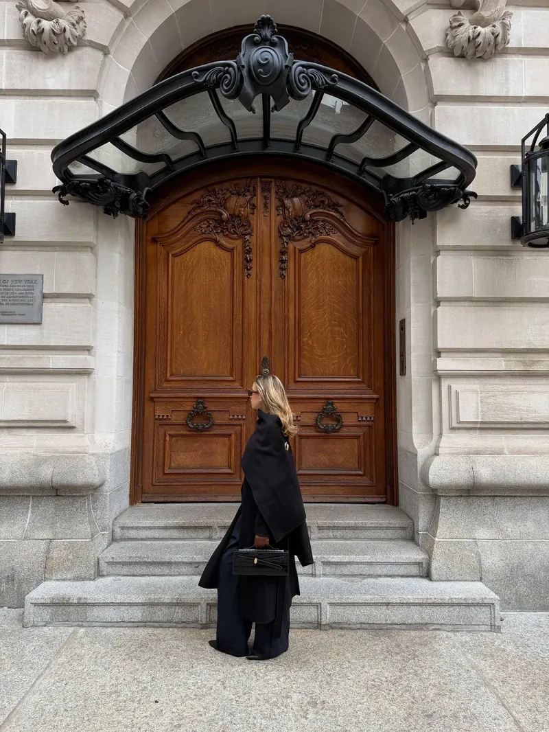 Annie in a long black coat at a carved wooden doorway