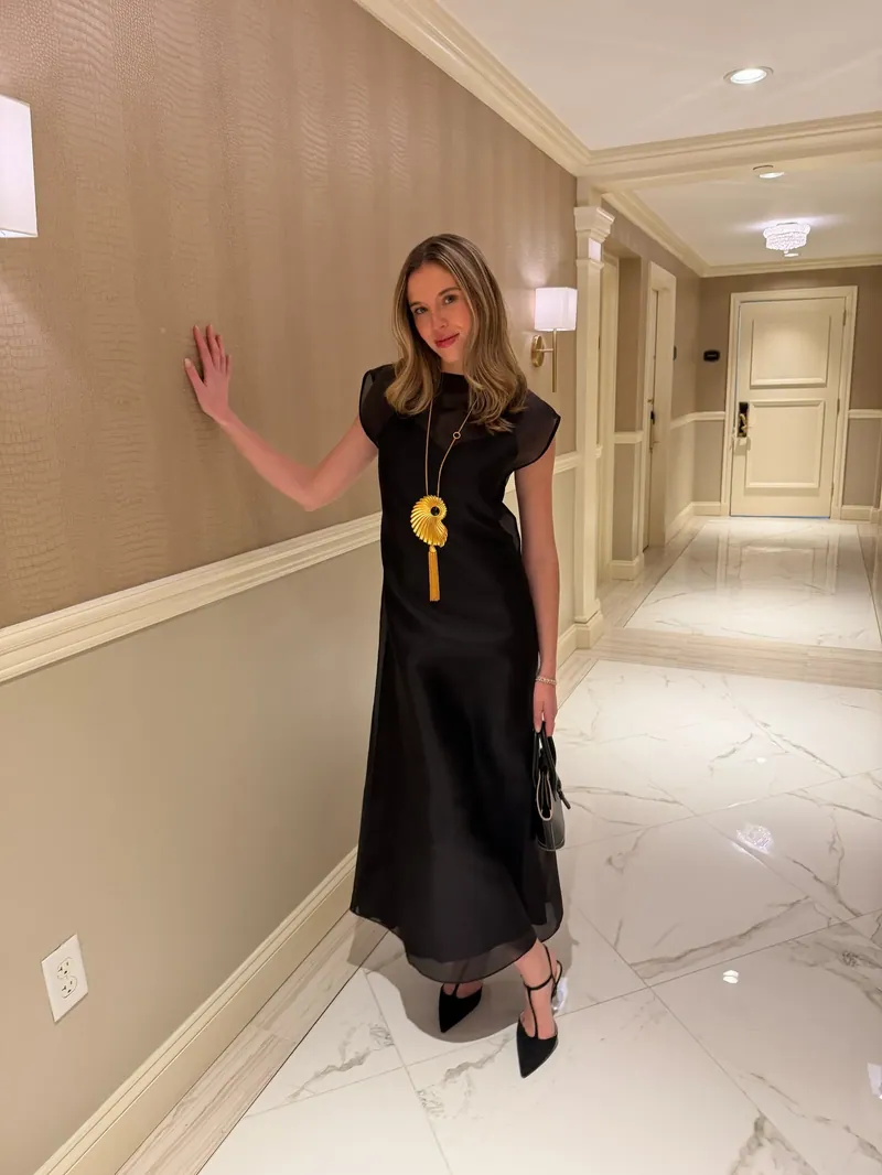 Annie in a long black dress and a gold shell necklace in a hotel hallway
