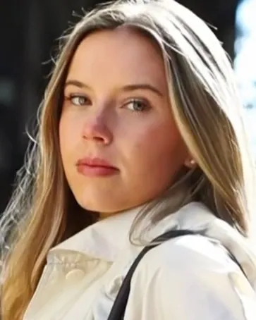 Annie in a white coat with a black bag strap on a sunny city street
