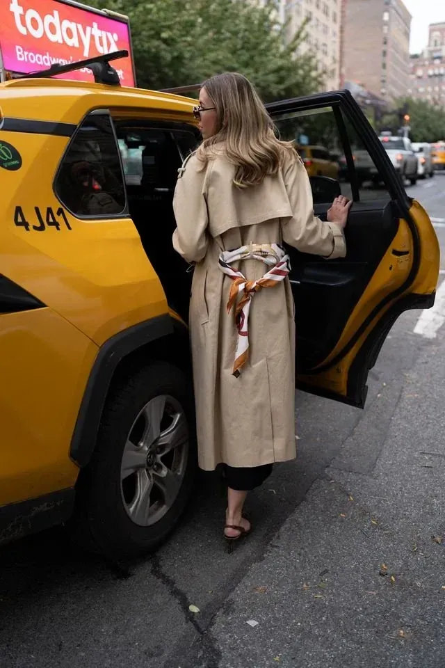 Annie stepping out of a yellow cab in a trench coat